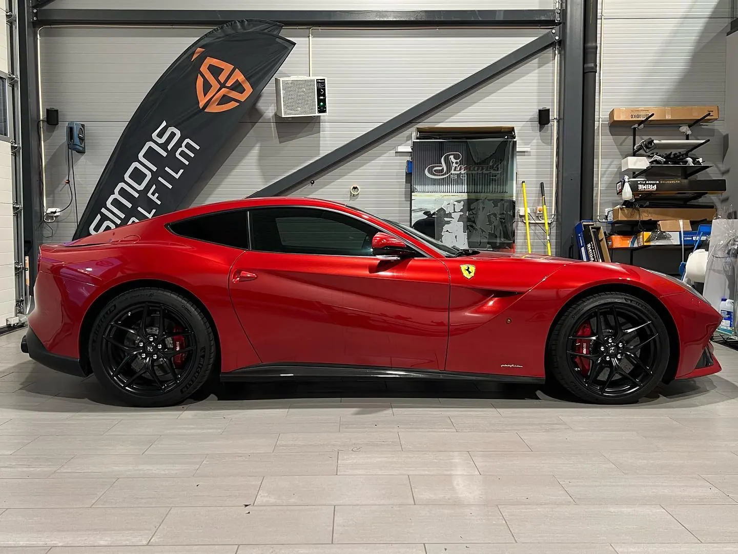 Rød Ferrari F12 i sideprofil foran Simons Solfilm-banner